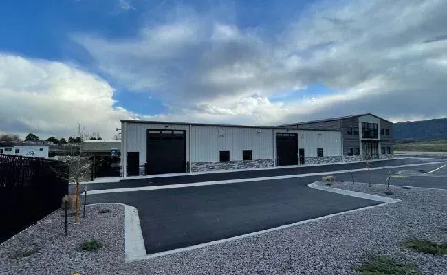 A modern, single-story industrial metal warehouse building with two large black garage doors and stone veneer siding.