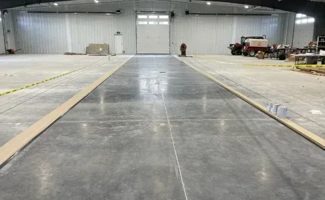 A polished concrete floor path runs through a wide, empty industrial warehouse space under construction.