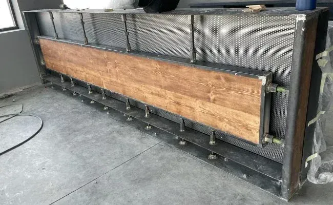 A metal framework structure with a wood panel insert, positioned on a concrete floor during construction.