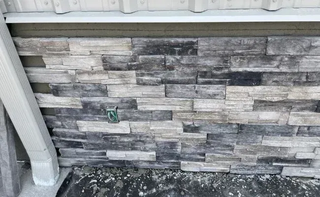 A partial exterior wall featuring horizontal gray and white stone veneer, with a light-colored downspout on the left.