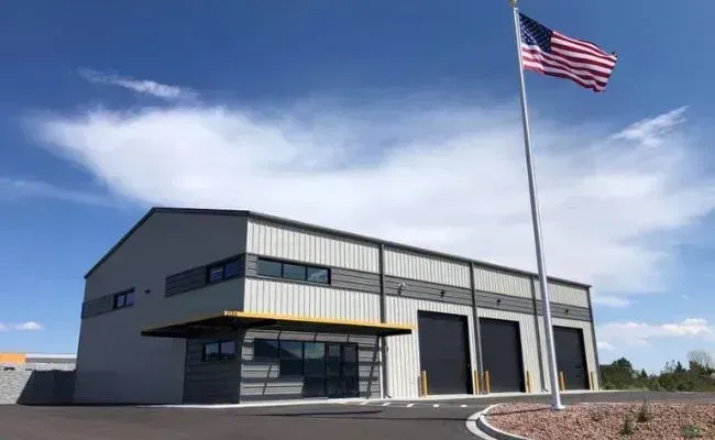 A modern, light gray metal commercial building with three large garage doors and a glass entryway under a blue sky.