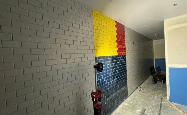 A room under construction featuring a wall partially tiled with grey, yellow, red, and blue bricks.