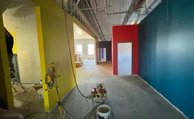 Interior of a room under construction with yellow and dark blue walls, a red section with a doorway, and equipment.
