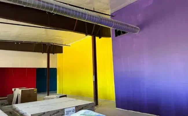 An interior space under construction with walls painted in vibrant solid colors: red, dark blue, yellow, and a purple gradient.