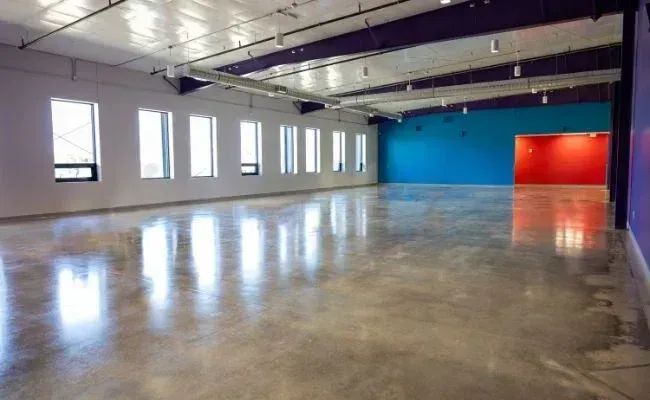 An empty room with polished concrete floors, white walls with a row of windows, and blue and red accent walls.