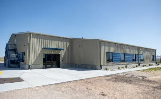 A tan, metal-sided commercial building with blue-trimmed windows, an entrance, and a dark metal external staircase.