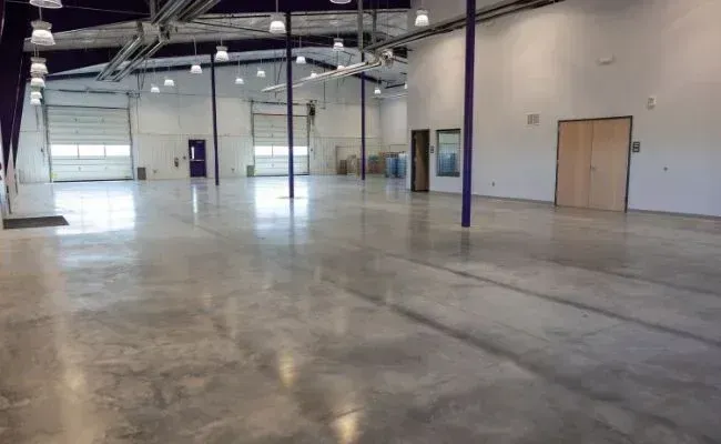 An expansive, empty warehouse interior with polished concrete floors, tall ceilings, and large bay doors.