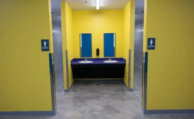 A bright yellow hallway with a dual-sink vanity, two mirrors, and separate restrooms on either side.