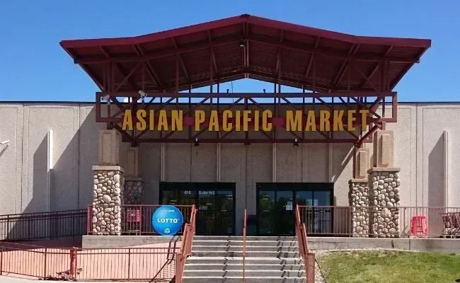 The entrance to an Asian Pacific Market store with a large metal awning and stone pillars under a clear blue sky.