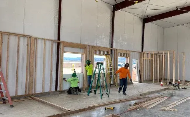Construction workers in safety gear framing an interior wall of a large building.
