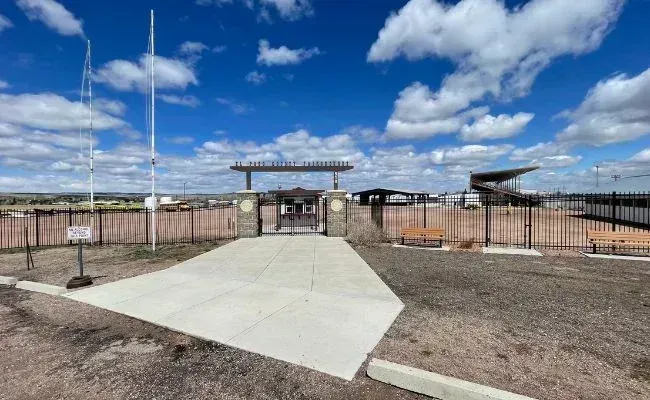 A wide shot of a gated entrance to an outdoor stadium or fairgrounds under a blue, cloudy sky.