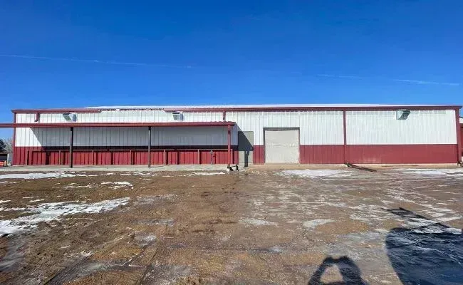 A long, rectangular metal warehouse building with white upper walls, red lower walls, and a covered front porch.