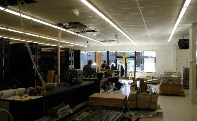 A commercial interior space under renovation with dark shelving units, construction materials, and people near an entrance.