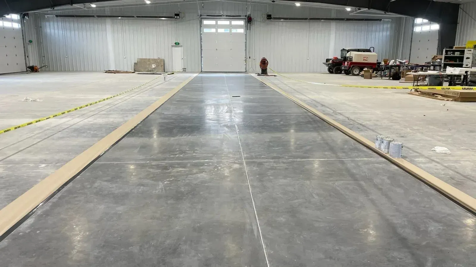 A wide, polished concrete floor stretches through a large, brightly lit warehouse with open bay doors.
