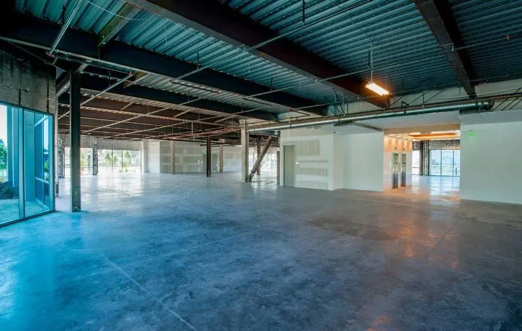 An open-plan commercial interior under construction with exposed metal ceilings, concrete floors, and steel beams.