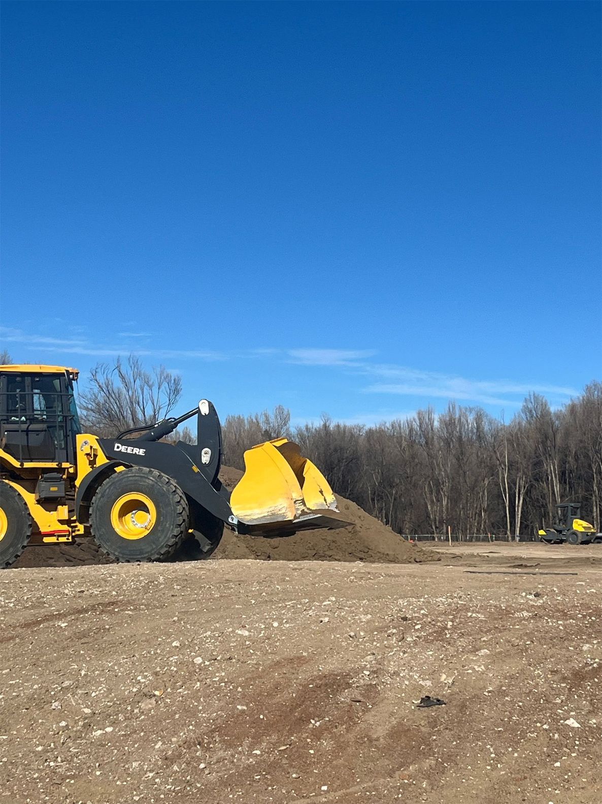 Yellow front loader moving dirt at a construction site under a clear blue sky.