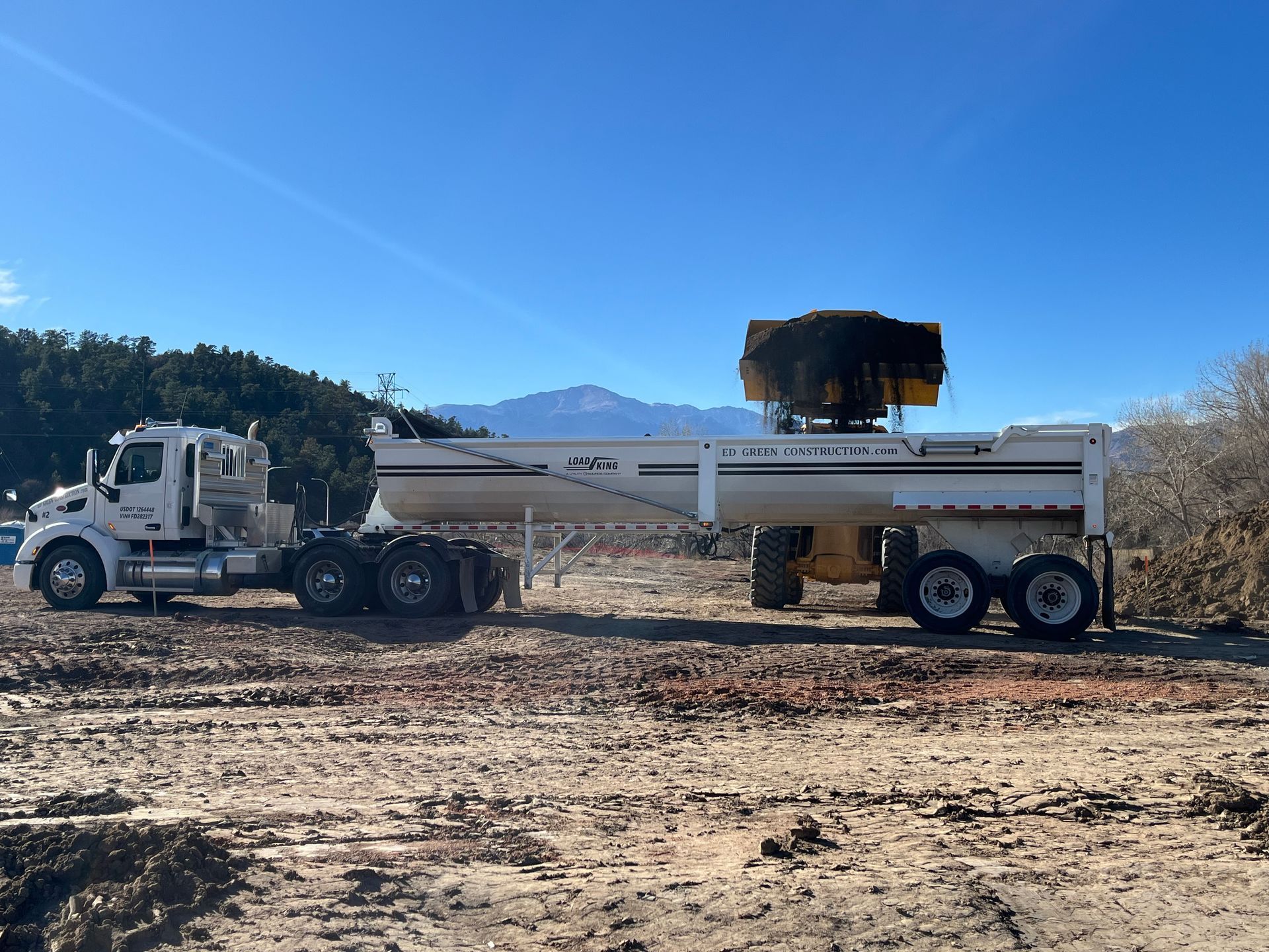 White dump truck with raised bed on a dirt construction site under a clear blue sky