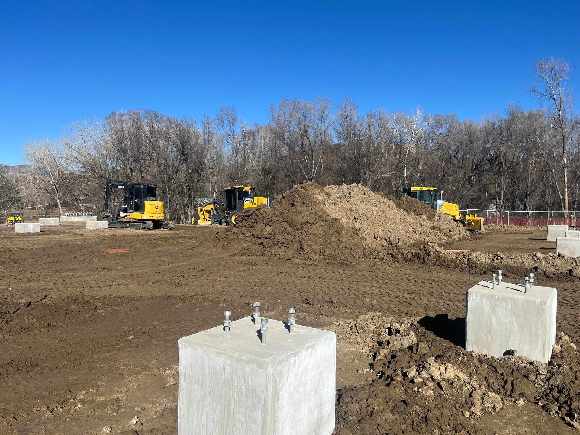 Construction site with bulldozers, dirt piles, and concrete foundations under a clear blue sky