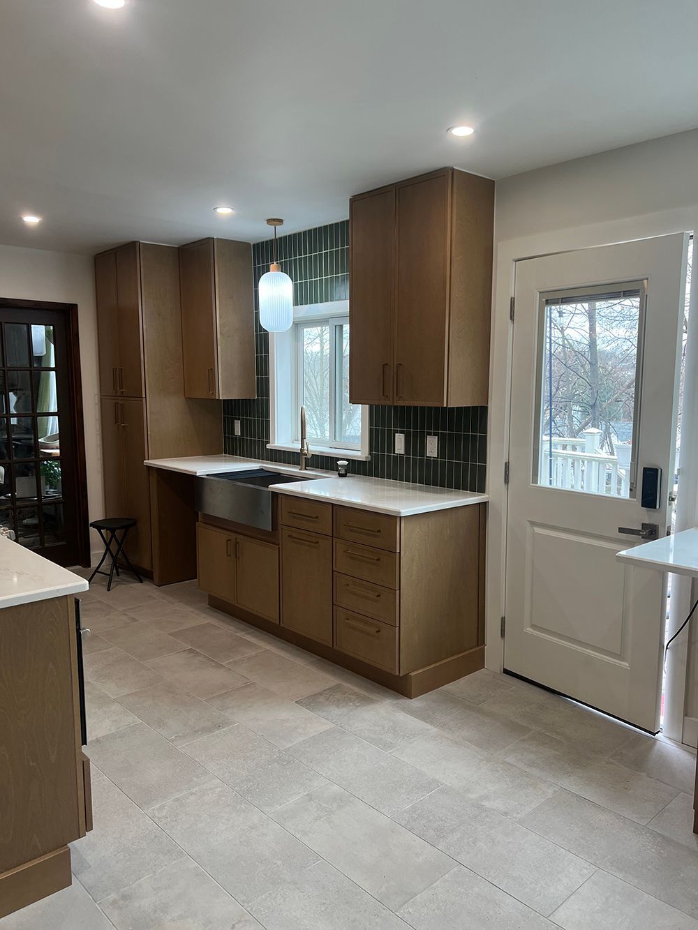 Modern kitchen with wood cabinets, light tile floor, white door, and recessed ceiling lights