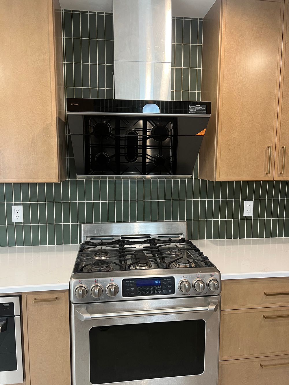 Modern kitchen with stainless steel stove and black microwave between wood cabinets and green tile backsplash