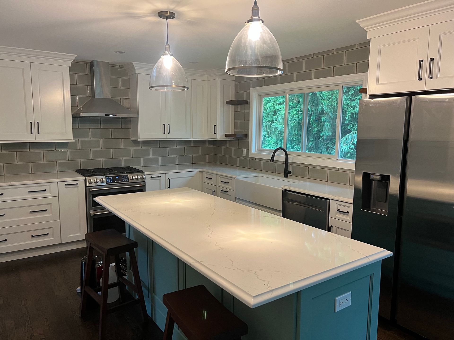 Modern kitchen with white cabinets, gray tile backsplash, stainless fridge, and a large island under pendant lights
