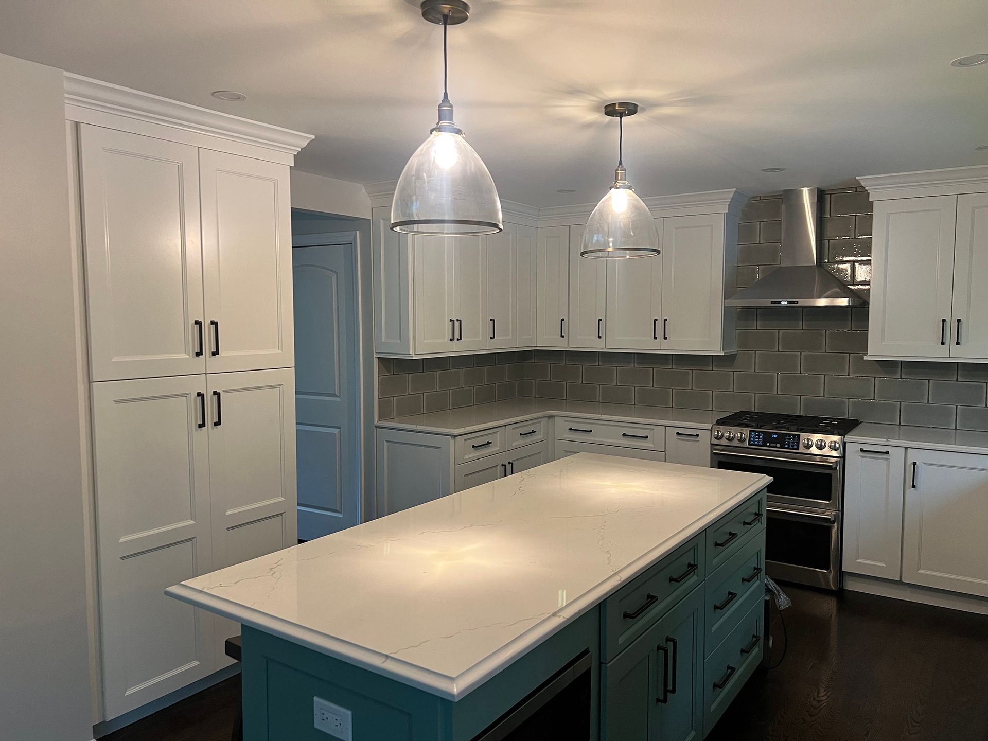 Bright modern kitchen with white cabinets, teal island, stainless range, and pendant lights