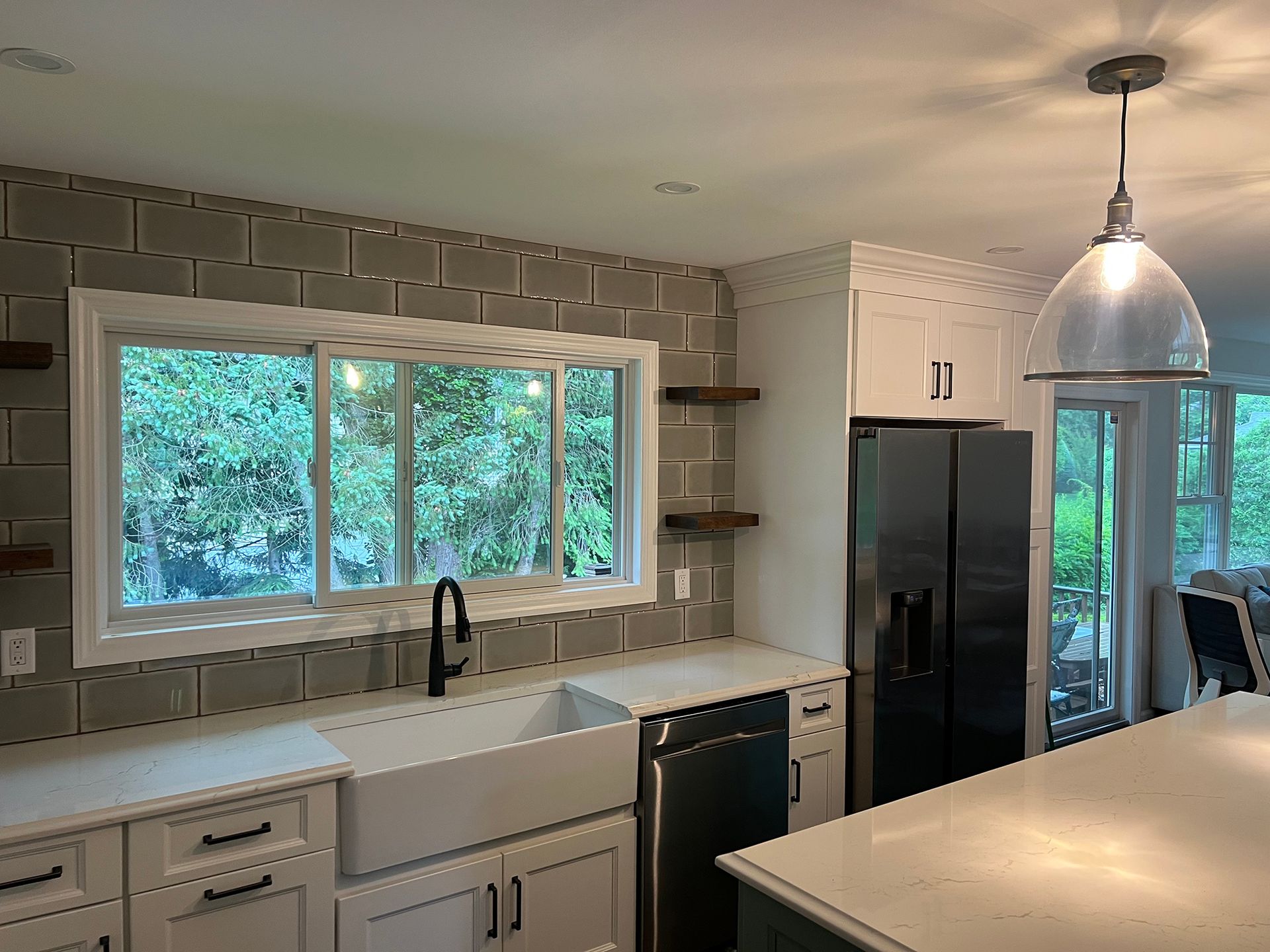 Modern kitchen with white cabinets, large window over sink, black fridge, and pendant light