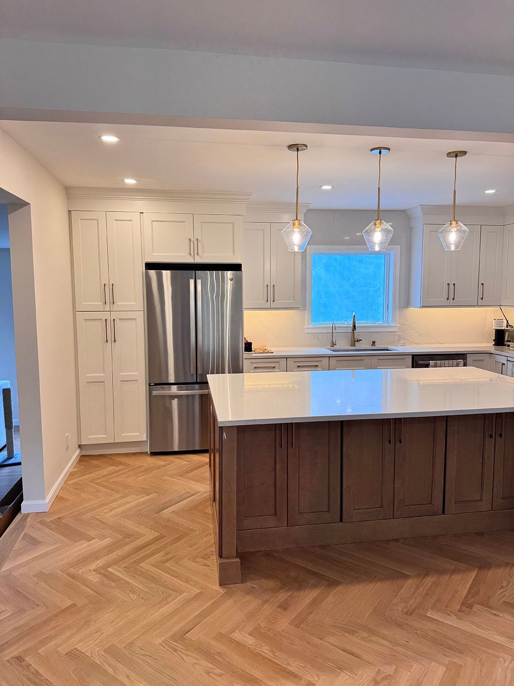 Bright modern kitchen with white cabinets, stainless fridge, and a dark wood island on herringbone floors.