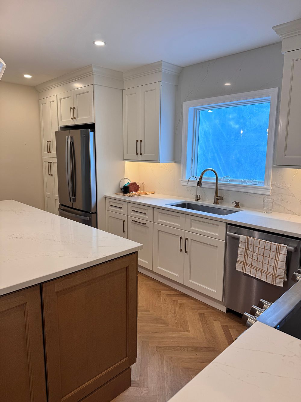 Bright white kitchen with stainless steel fridge, herringbone floor, and window over the sink.