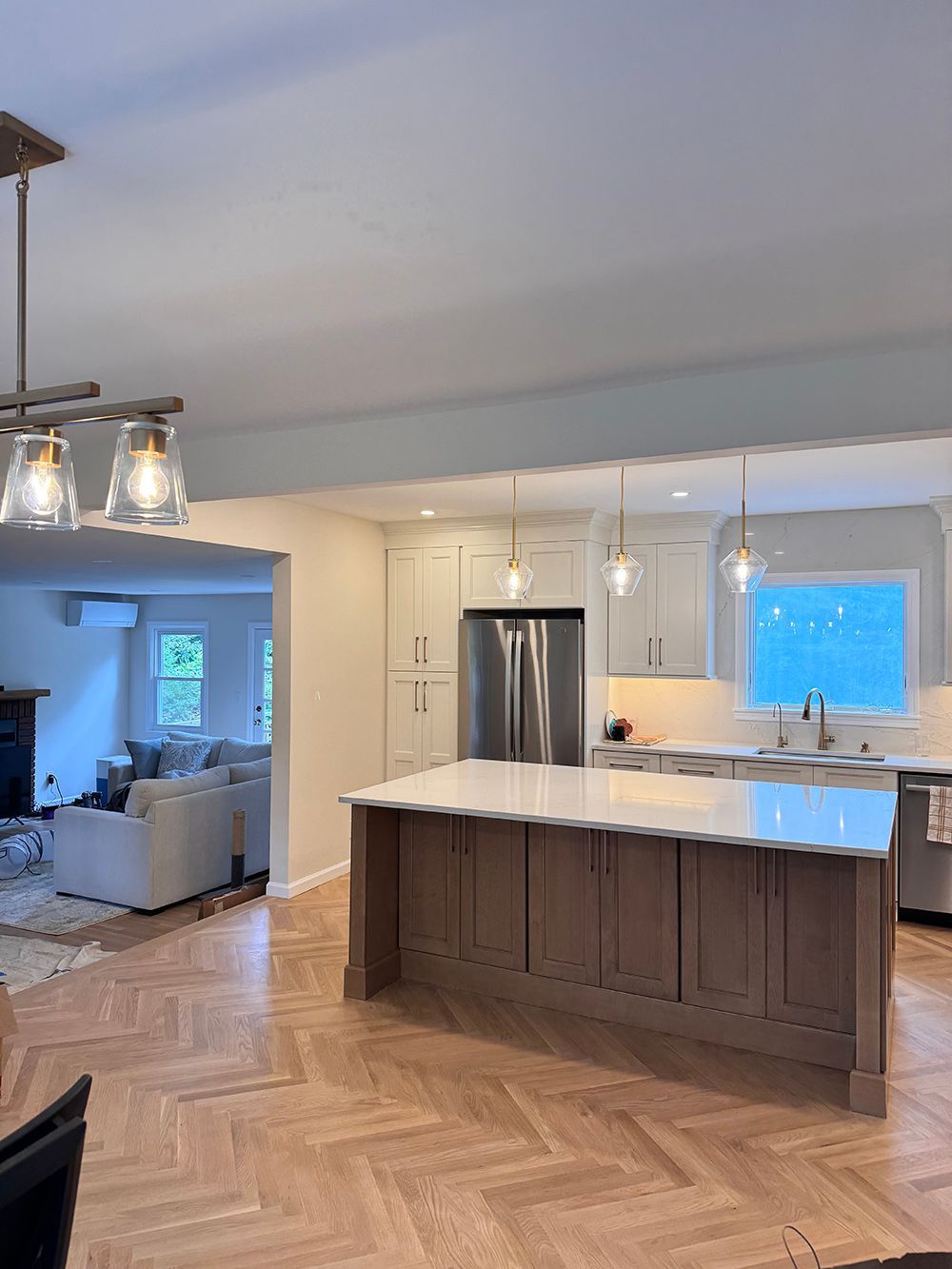Bright modern kitchen with island, stainless fridge, pendant lights, and herringbone wood floor