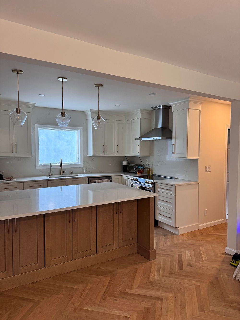 Bright kitchen with white cabinets, pendant lights, and a large island over herringbone wood flooring.