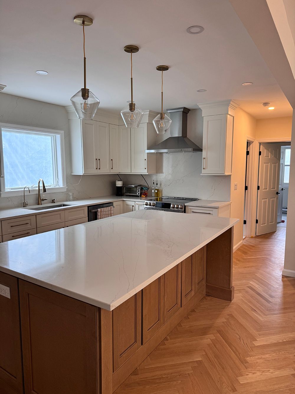 Bright kitchen with white island, wooden cabinets, herringbone floor, and pendant lights