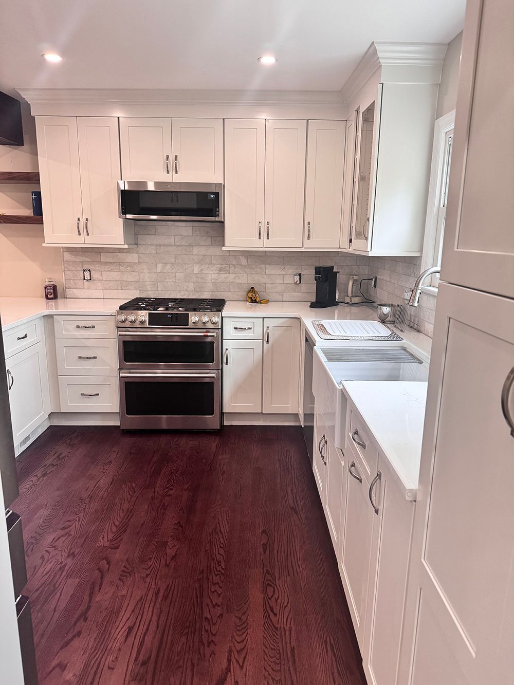 Bright white kitchen with stainless steel stove, white cabinets, and dark wood floors.