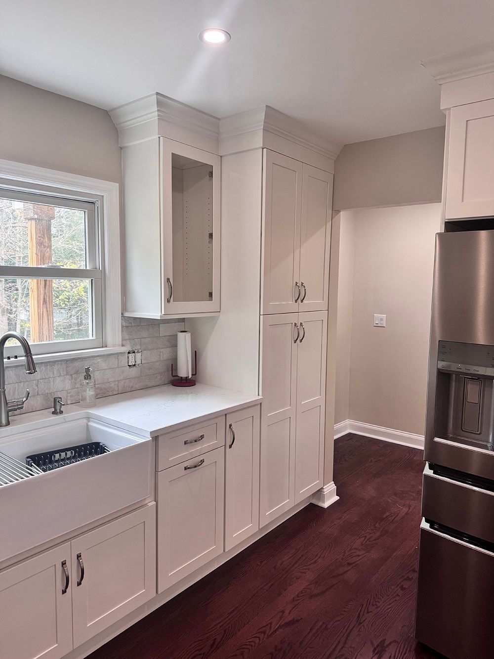 Bright white kitchen with quartz counters, marble backsplash, tall cabinets, and a stainless steel fridge.