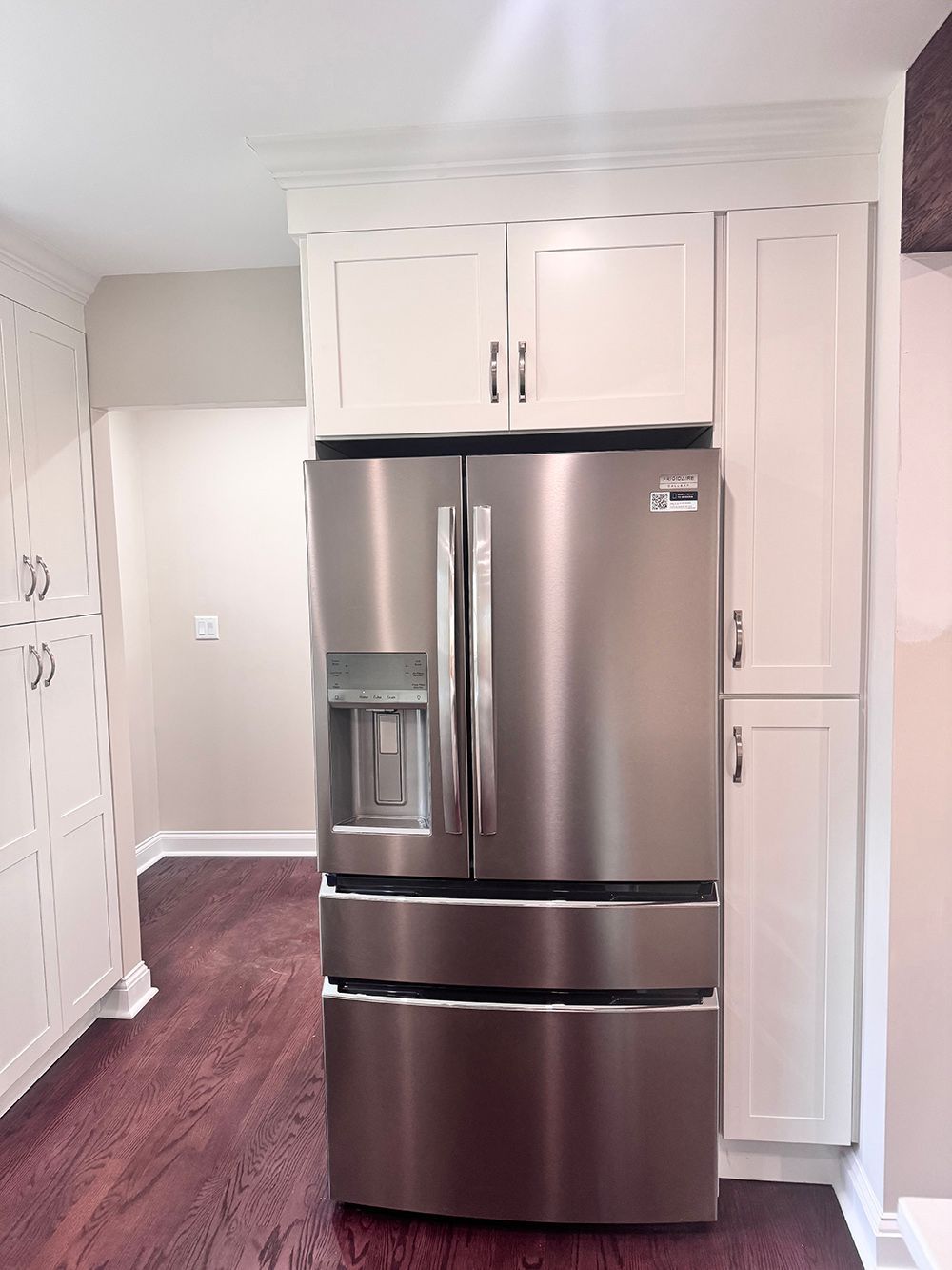 Stainless steel French-door refrigerator in a bright kitchen with white cabinets and dark wood floor