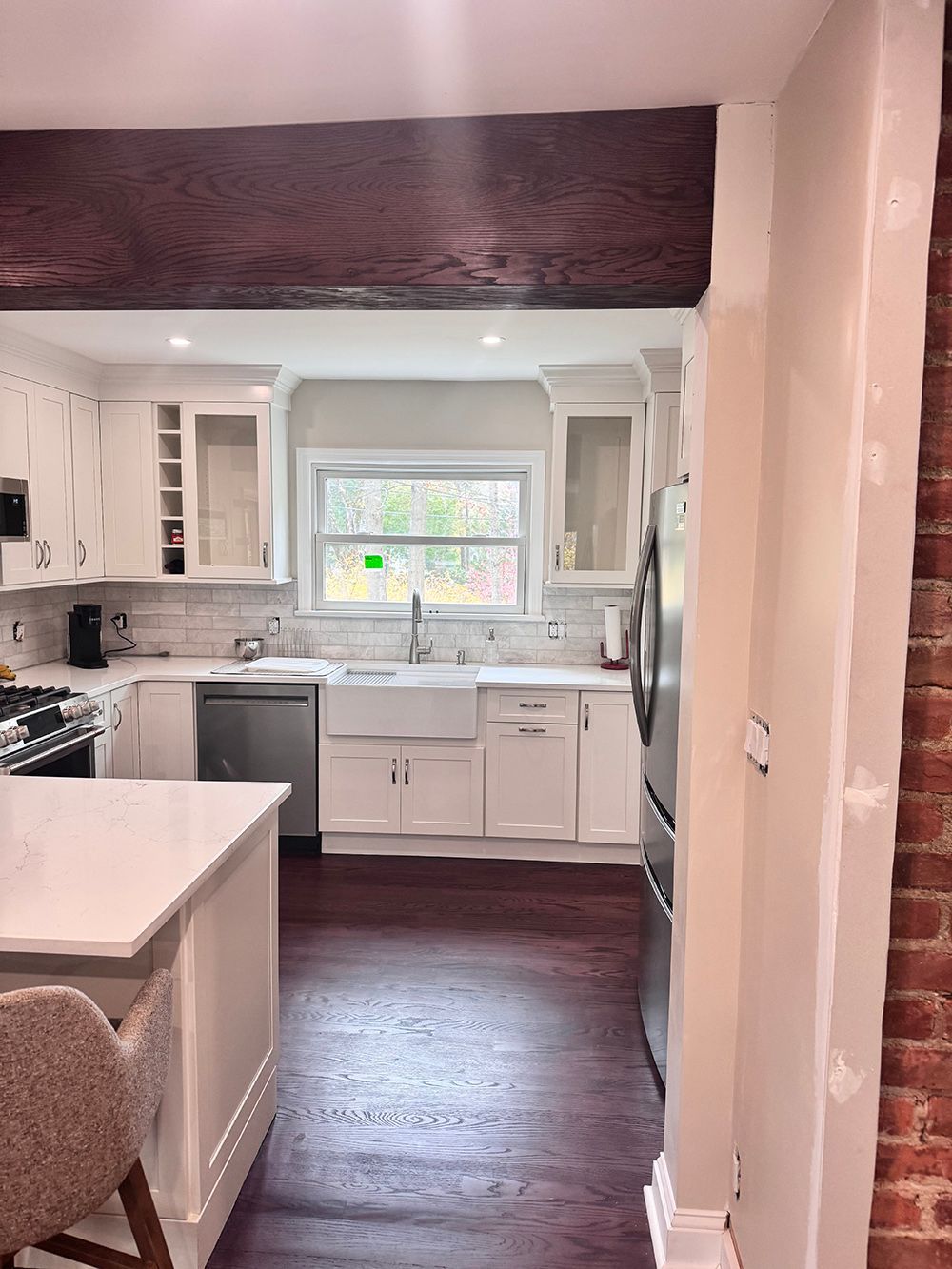 Bright white kitchen with dark wood floor, central sink under a window, and a large dark wood beam overhead.