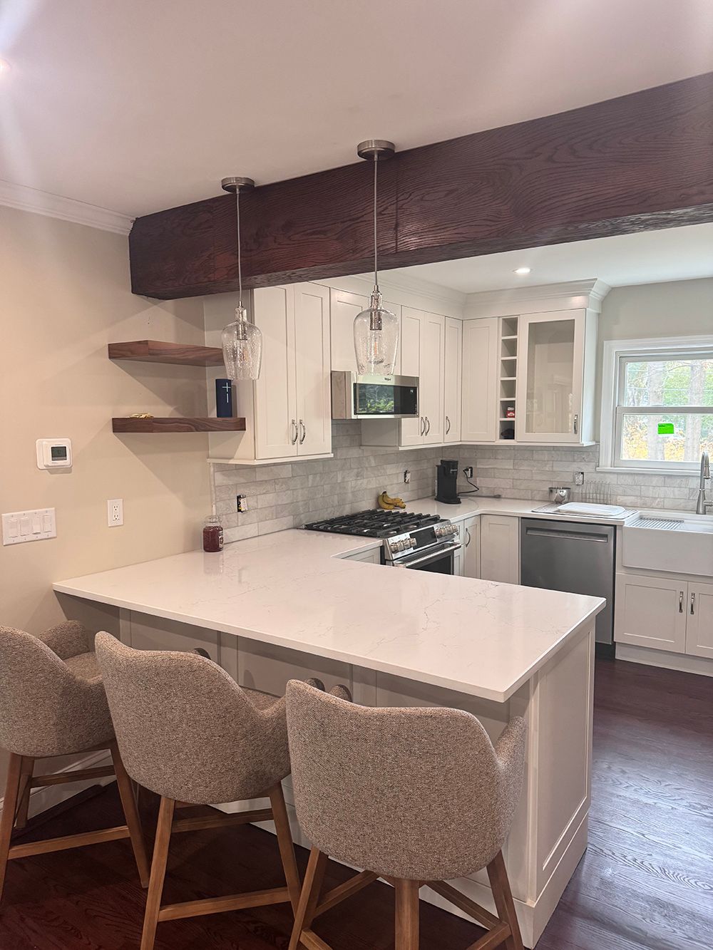 Bright kitchen with white island, beige stools, and dark wood beam overhead.