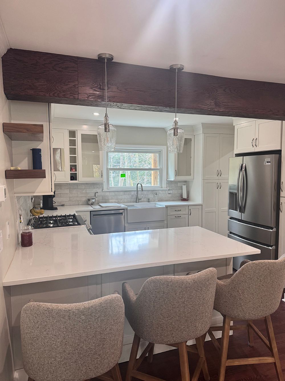 Modern kitchen with white island, bar stools, stainless steel fridge, and window above the sink.