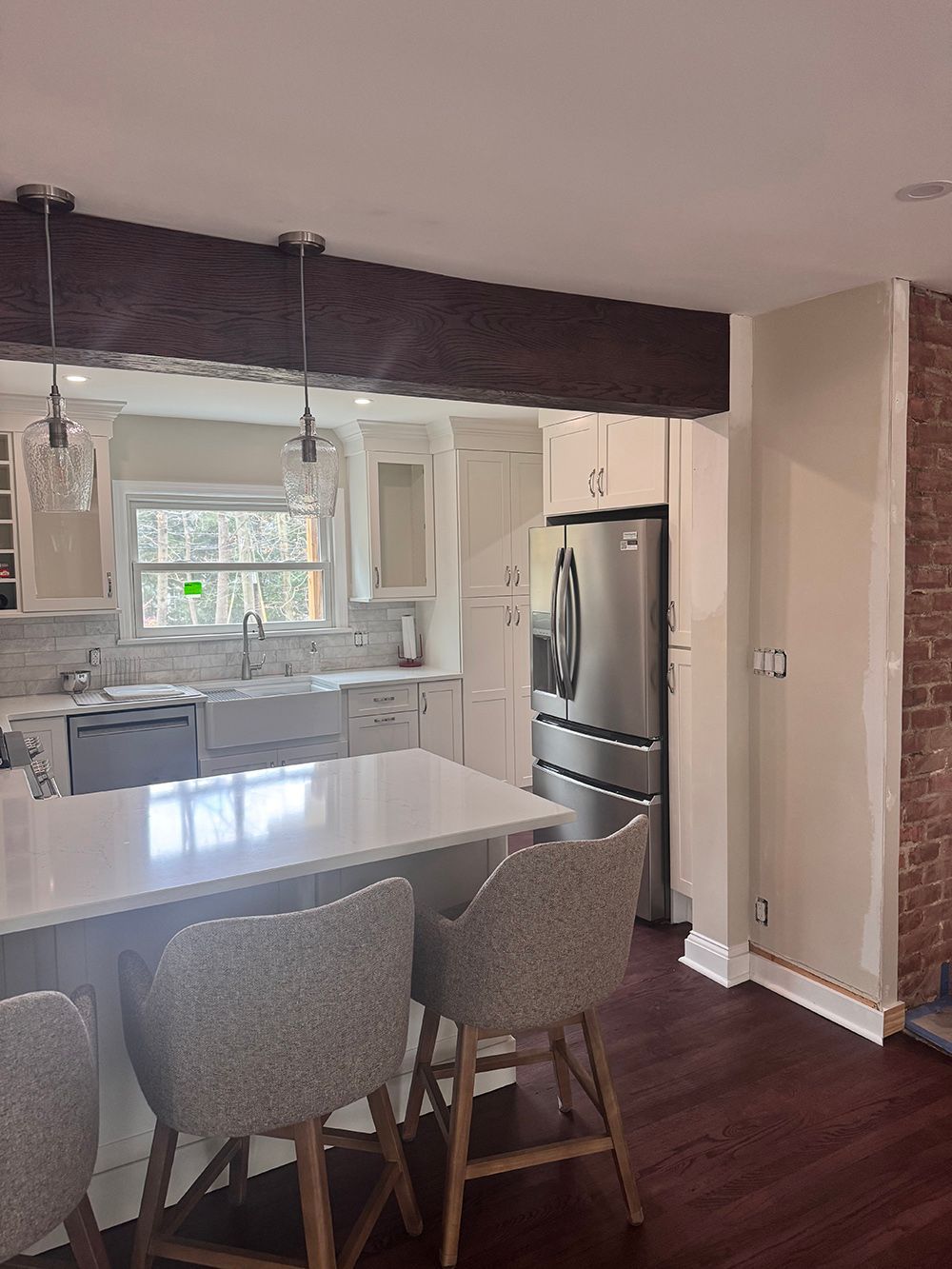 Bright kitchen with white island, gray chairs, stainless fridge, and dark wood floors