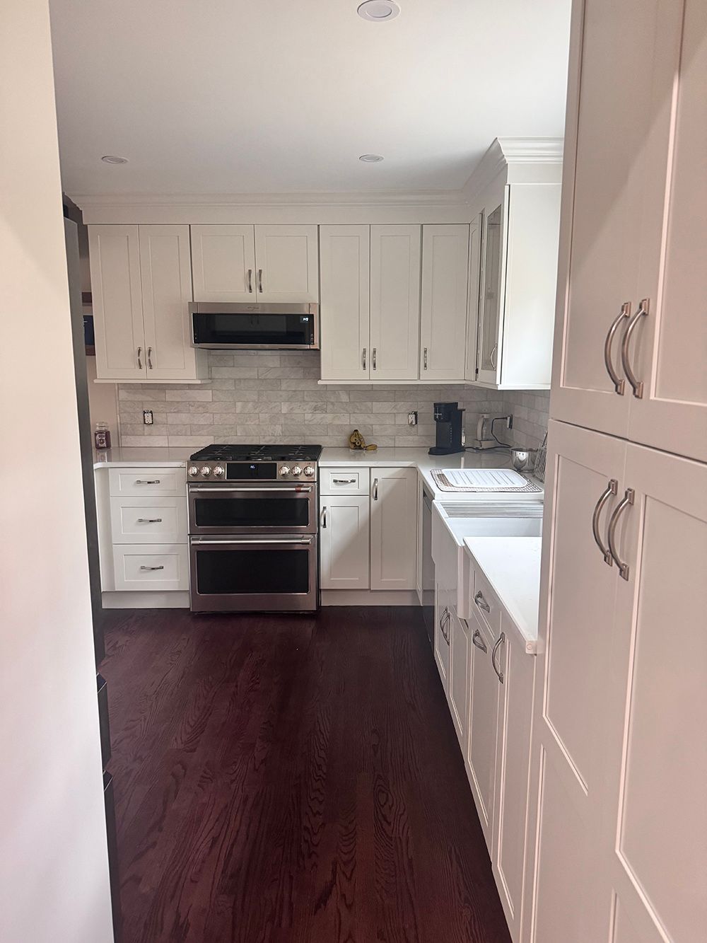 Narrow white kitchen with stainless stove, gray tile backsplash, and dark wood floor