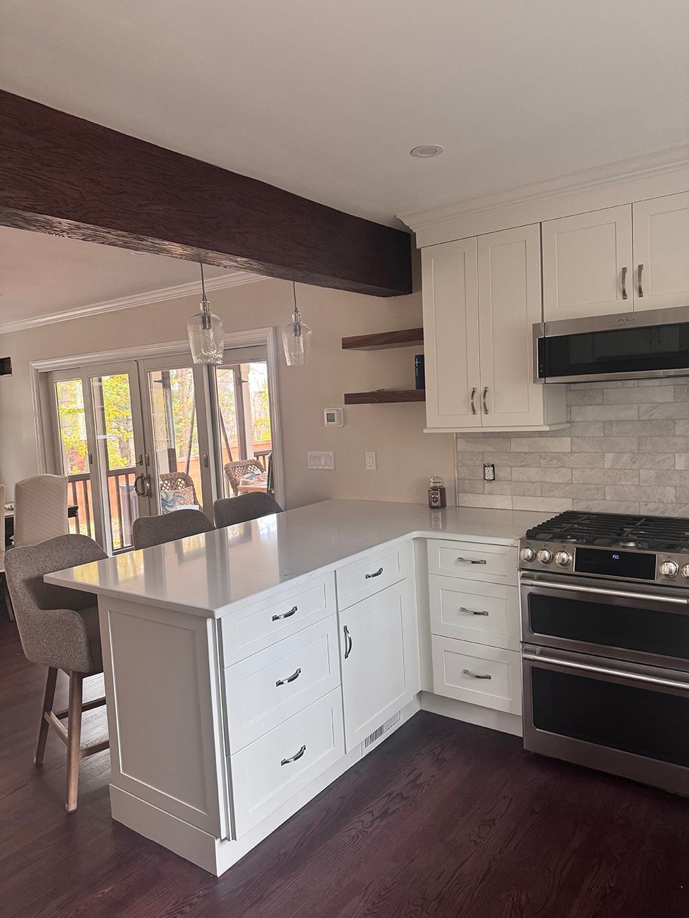 Bright white kitchen with island, stainless stove, dark wood floors, and large windows overlooking trees