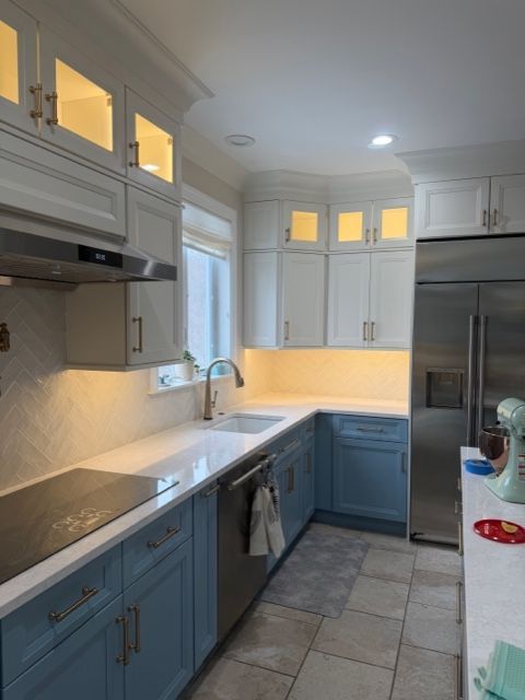 Bright kitchen with blue lower cabinets, white uppers, stainless appliances, and under-cabinet lighting.