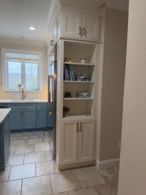 Bright kitchen with white cabinets, blue lower drawers, tiled floor, and a built-in pantry shelf.