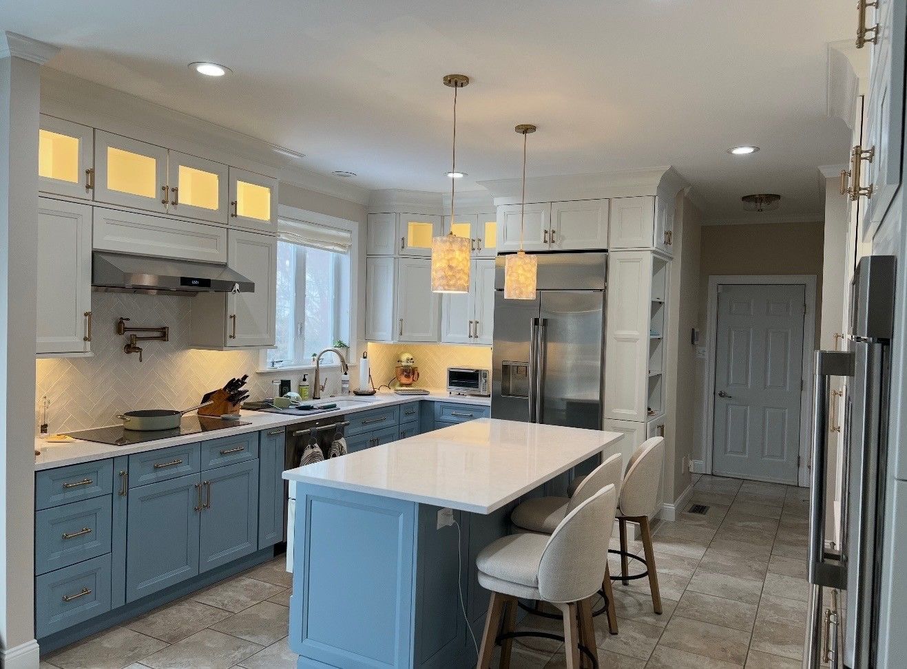 Bright modern kitchen with blue cabinets, white island, pendant lights, and stainless steel appliances.