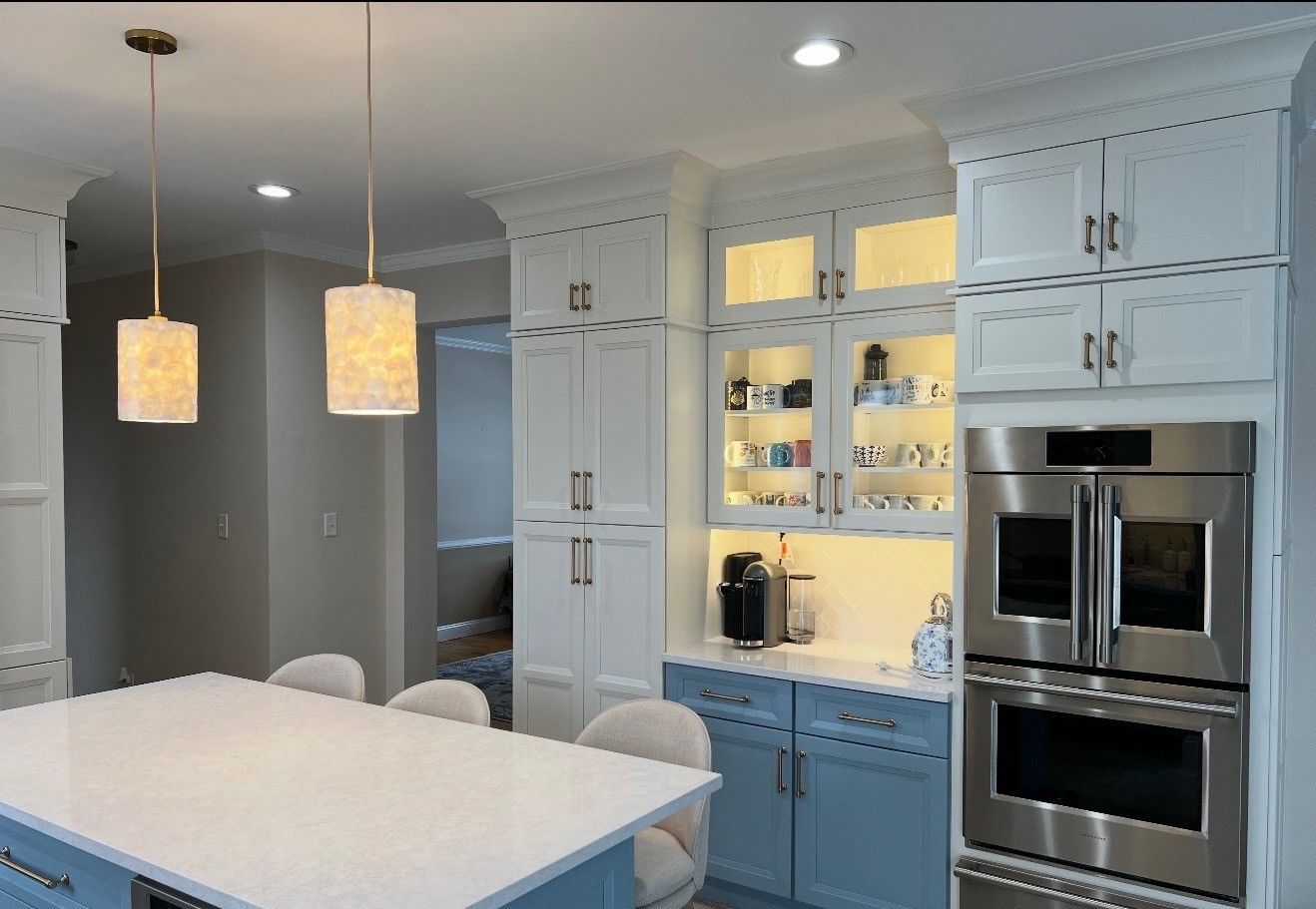 Bright modern kitchen with white cabinets, blue lower cabinets, island, pendant lights, and built-in ovens