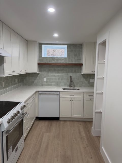Modern white galley kitchen with light wood floor, stainless appliances, and a small window above the sink