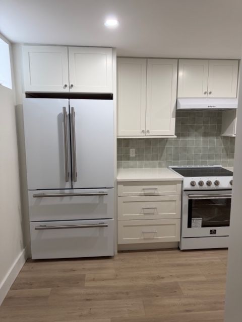 Small modern kitchen with white cabinets, stainless steel refrigerator, stove, and light wood flooring