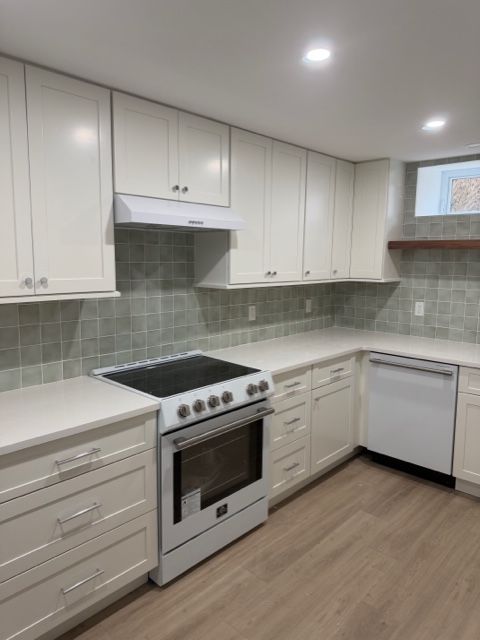 Bright white modern kitchen with stove, dishwasher, cabinets, and light wood flooring.