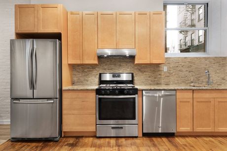 Modern kitchen with stainless steel refrigerator, stove, and dishwasher, light wood cabinets, and granite backsplash