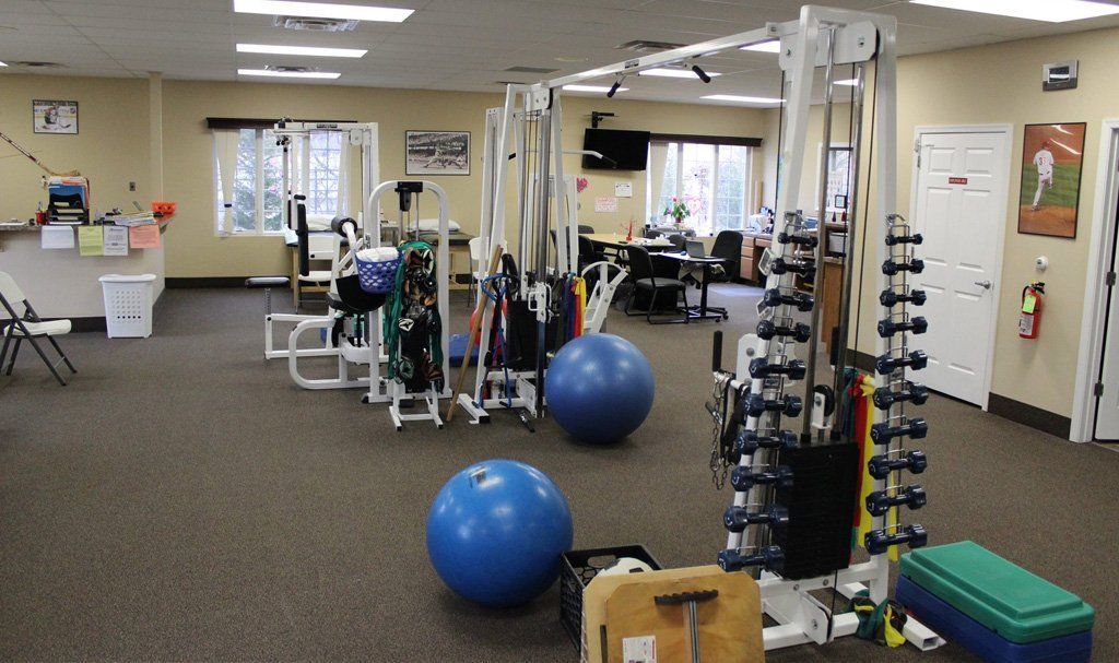 Inside a physical therapy clinic: exercise equipment, blue stability balls, and weights on racks.